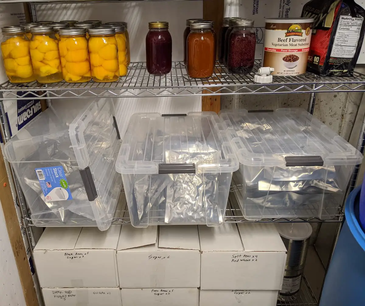 An Image of some of the freeze-dried foods in our pantry including home-canned peaches, jams, freeze-dried foods in individually marked mylar bags inside tubs, and commercially purchased food storage in white boxes.
