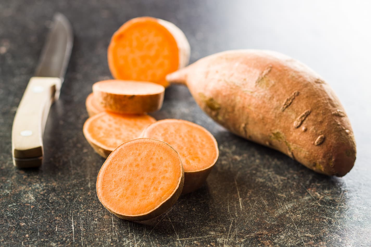 An image of sliced raw-cut sweet potatoes and a cutting knife.