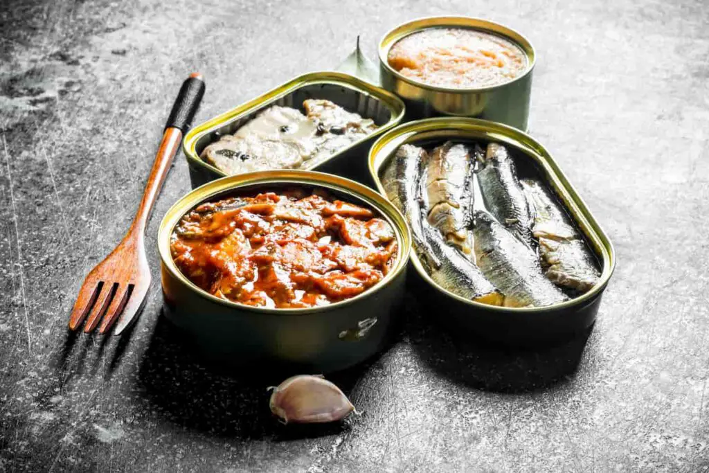 An image of Canned fish in tin cans on a dark rustic background.