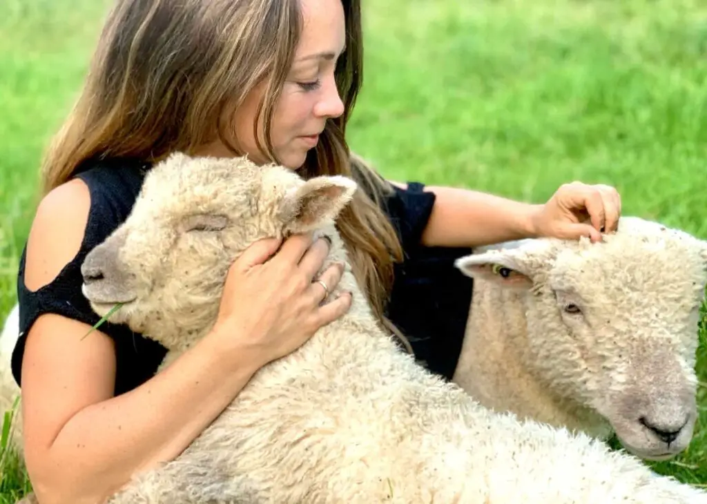 An image of a lady hugging and cuddling a sheep in the meadow.