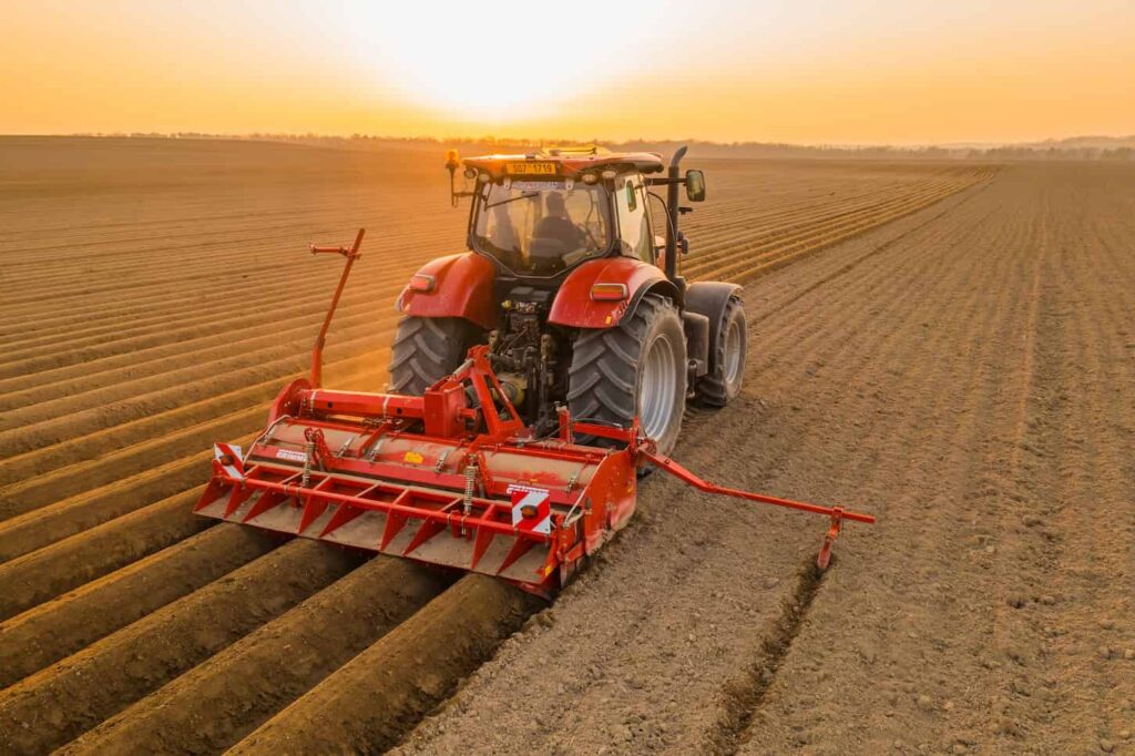 An image of a red Tractor harrowing in the field, dragging plow on purified soil.