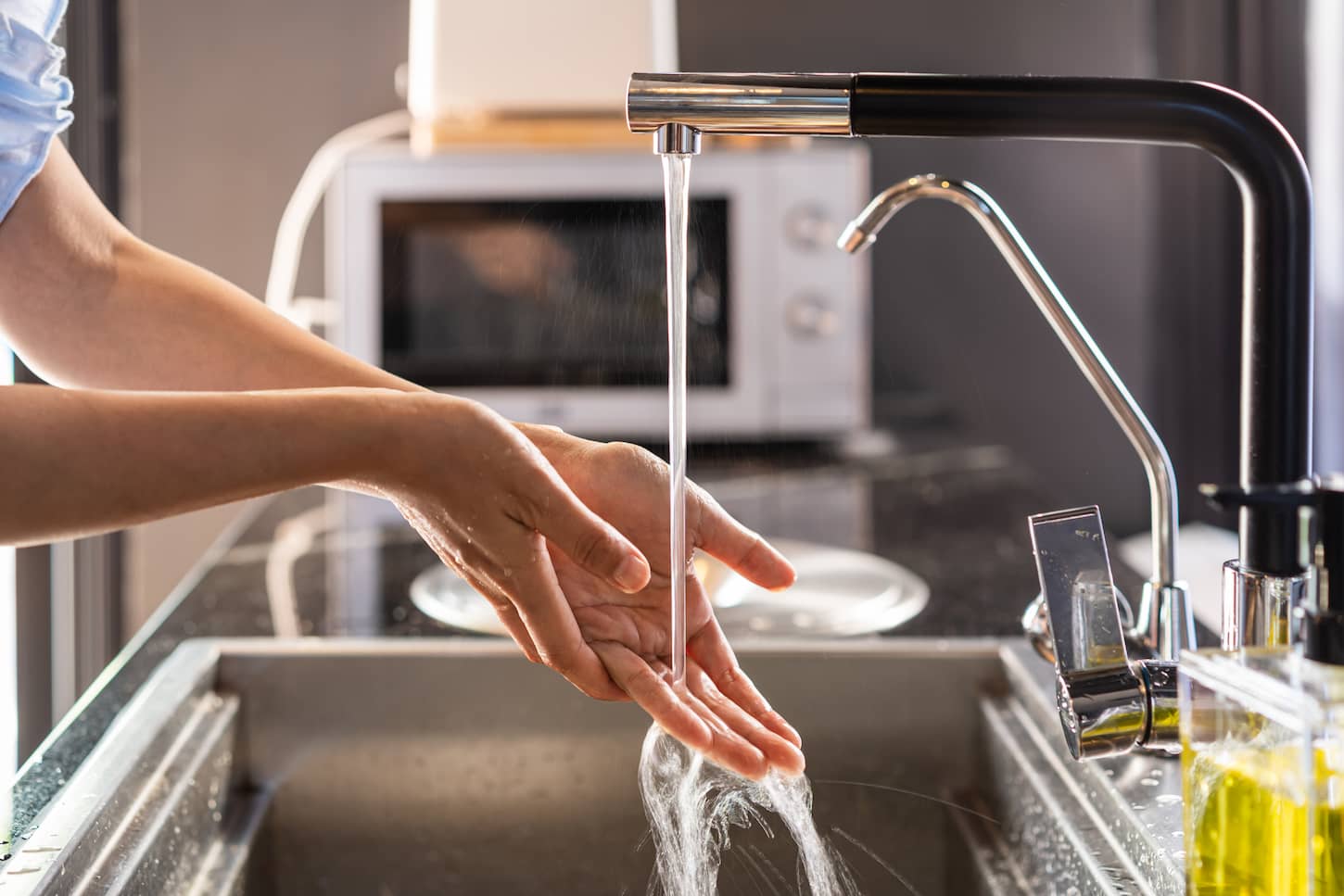 An image of a woman washing her hands in a running water in the kitchen sink at home.