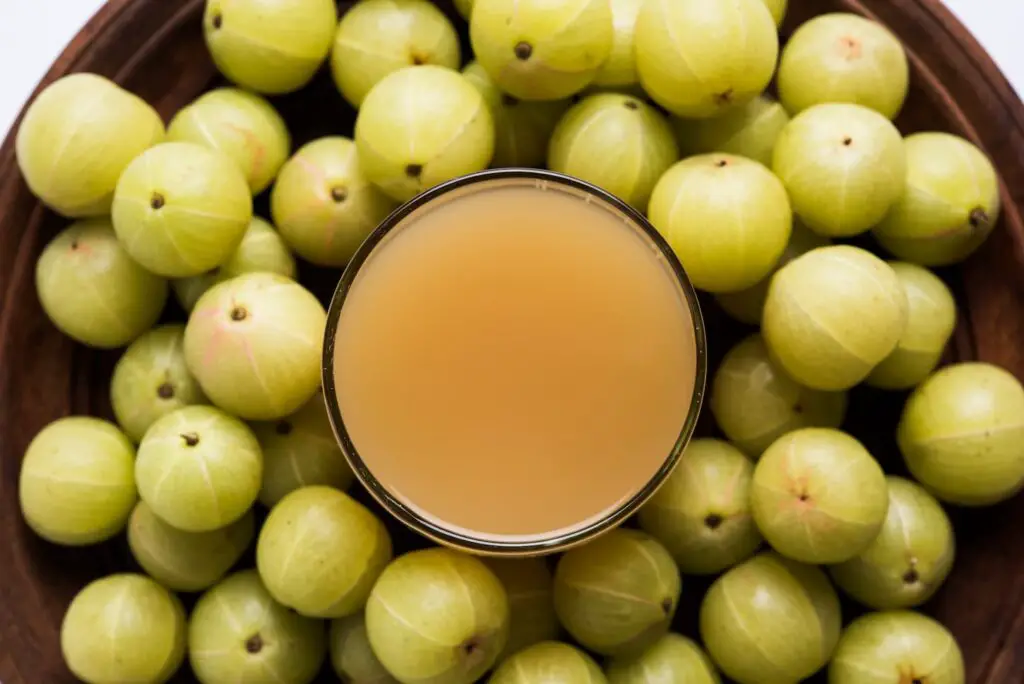 An image of fresh Gooseberry or Amla Juice (Phyllanthus emblica). Poured In a glass with whole Avla.