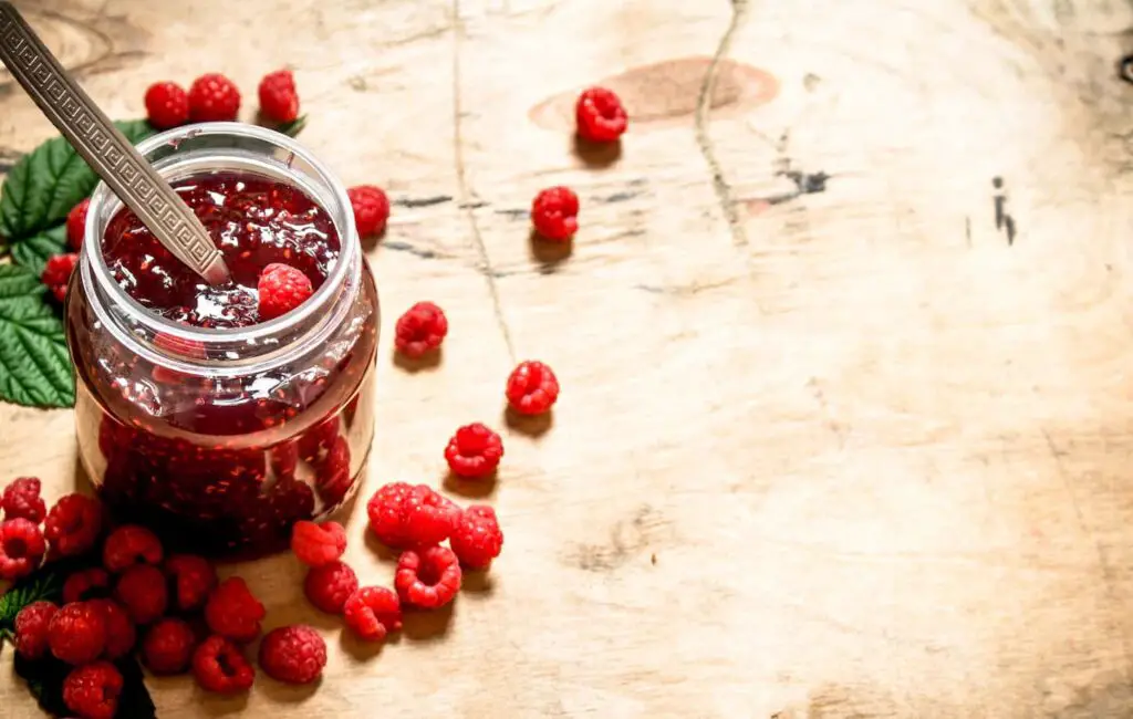 An image of Sweet jam with raspberries on a wooden table.