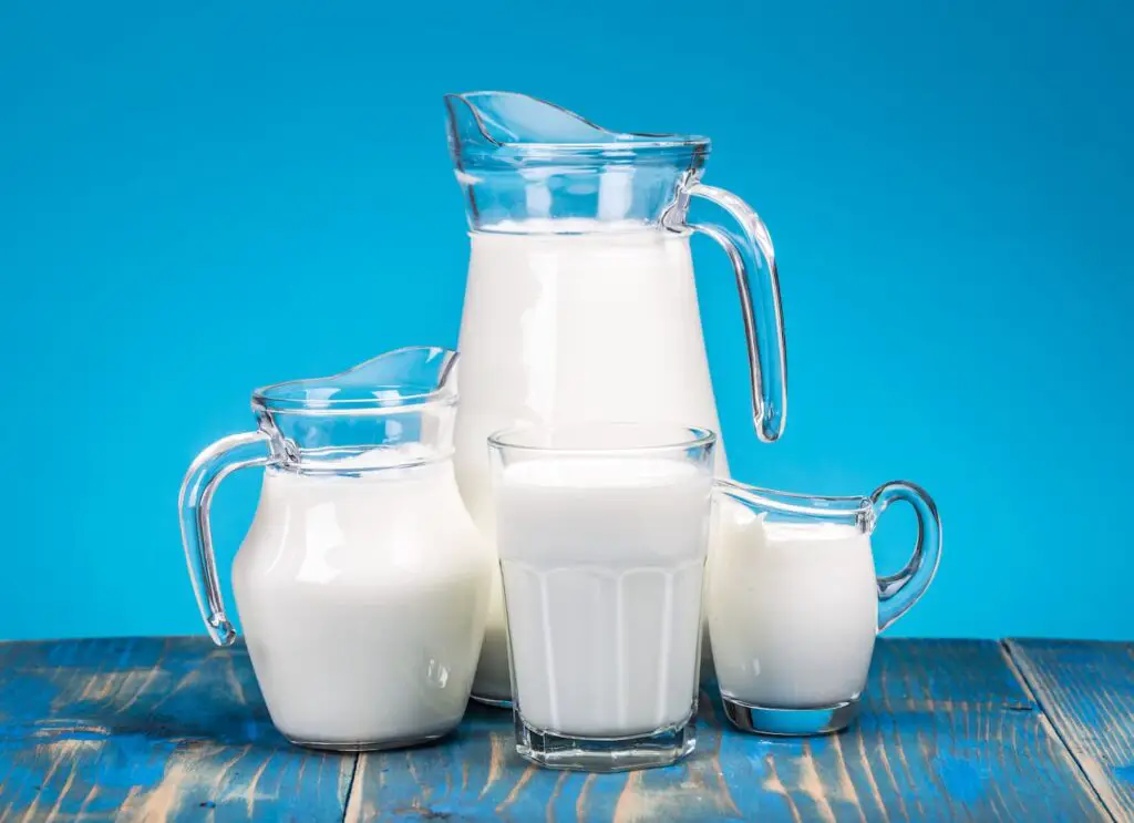 An image of glass pitchers with fresh milk on it on a blue background.