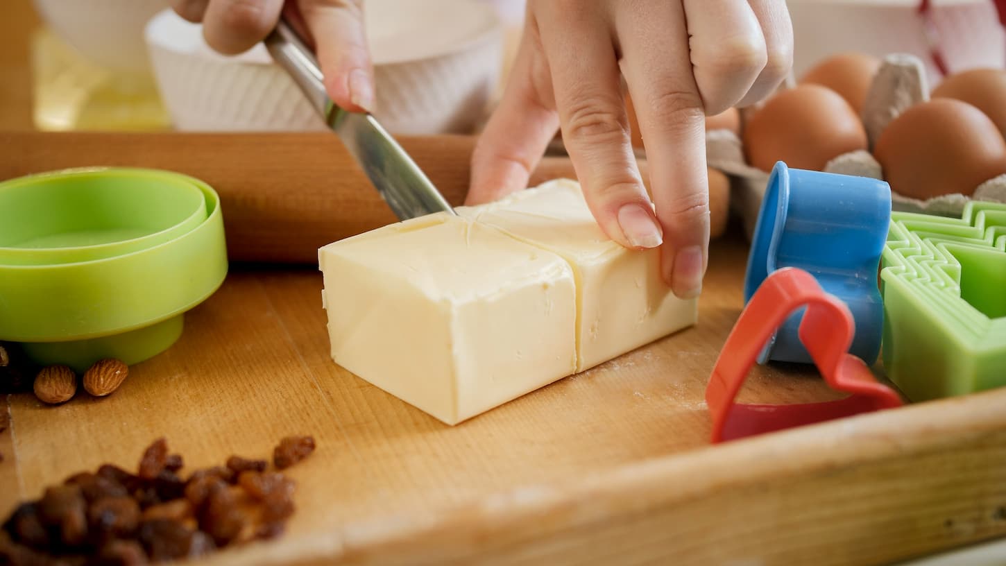 An image of a woman cutting butter for cooking pie or cake.