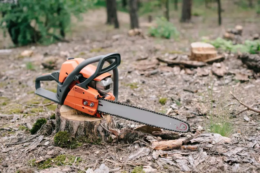 An image of an orange chainsaw on top of a freshly cut wood trunk.