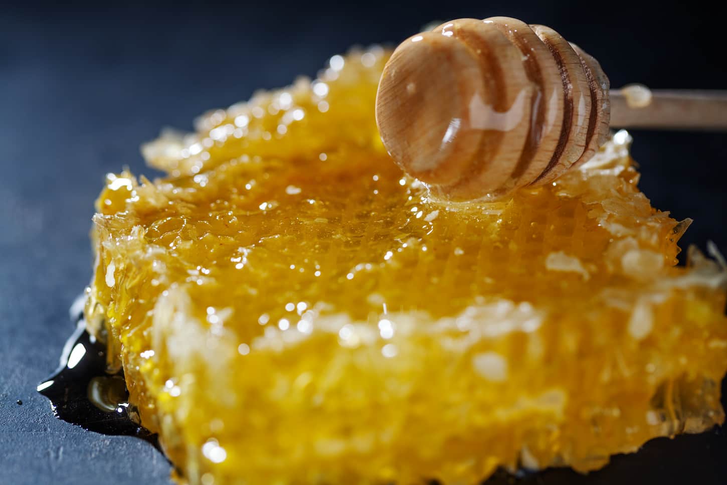 An image of a raw crystallized honeycomb and honey dipper on a dark background.