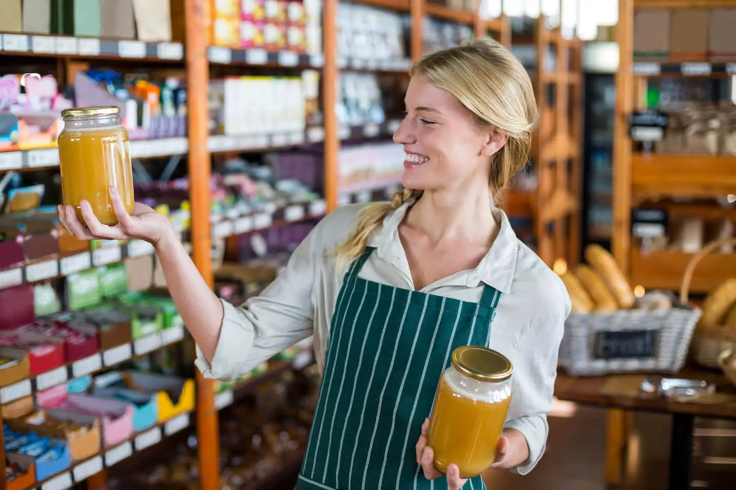 An image of a smiling female staff holding jars of honey in the supermarket store.