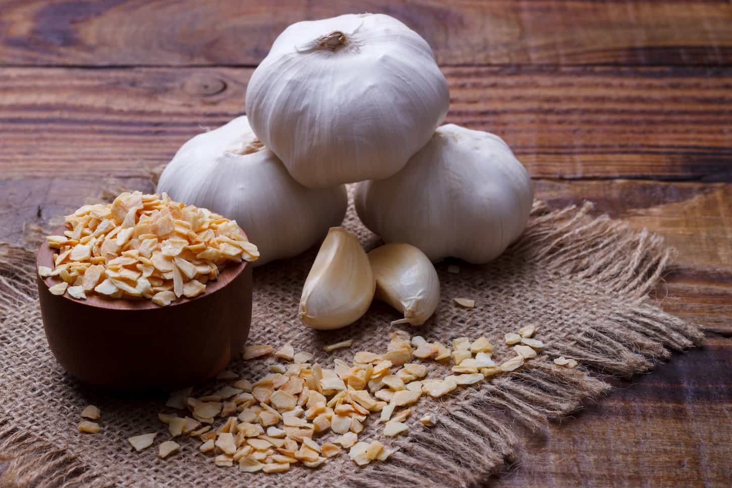 An image of a dried and fresh garlic on a wooden table.