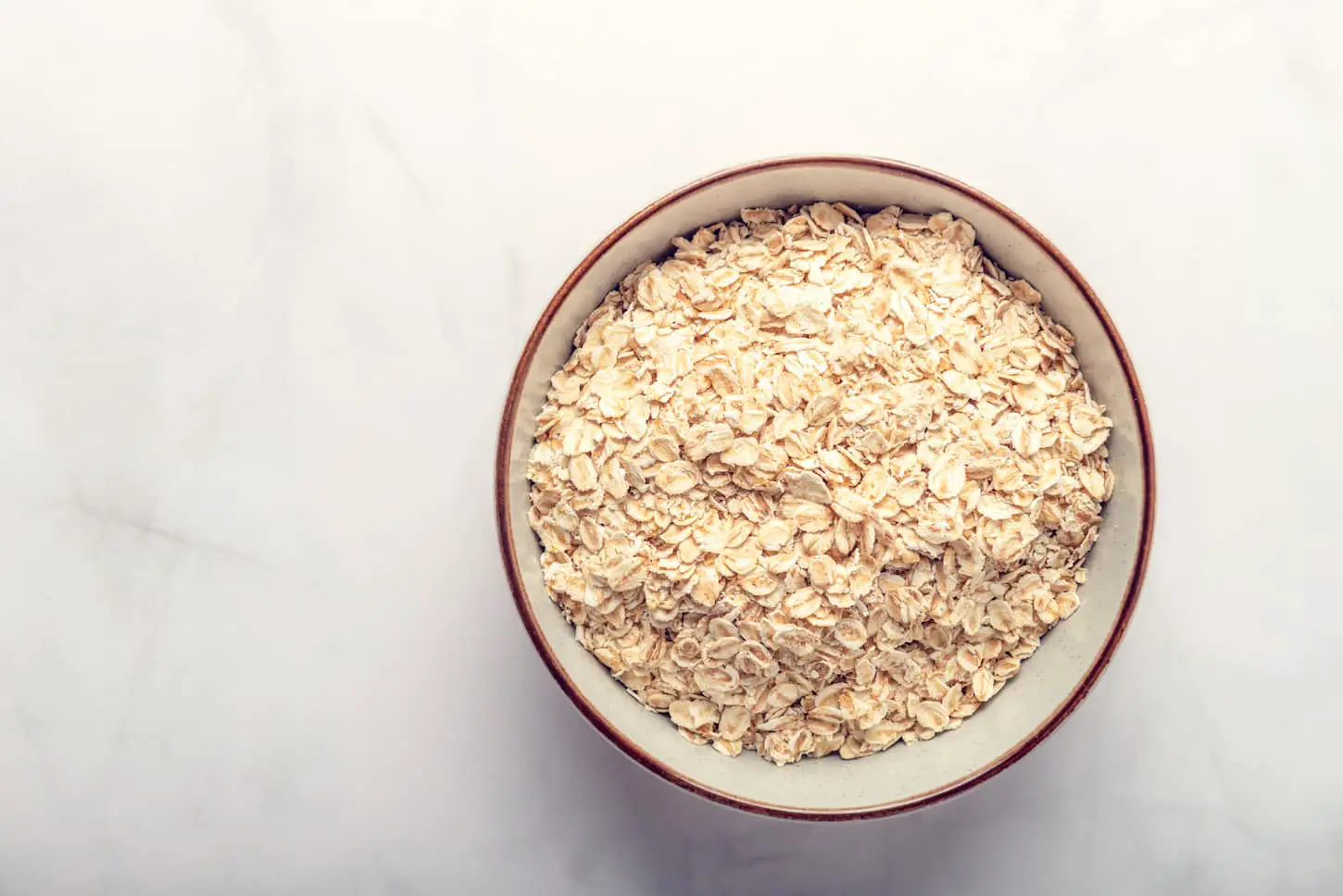 An image of Gluten-Free Rolled whole grain oats in a bowl on a marble background.