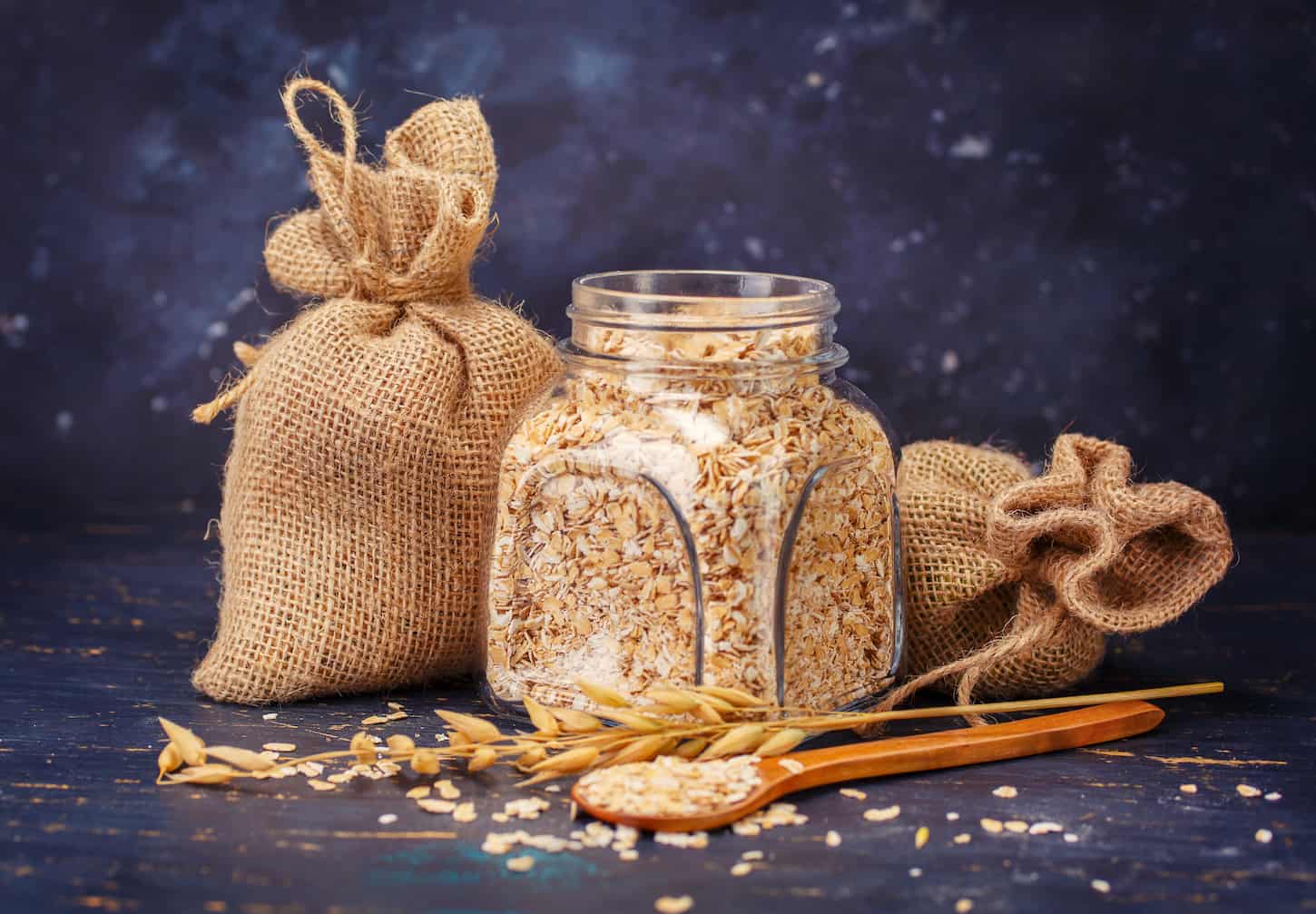 An image of Oatmeal in a glass jar and jute bags on a dark background.