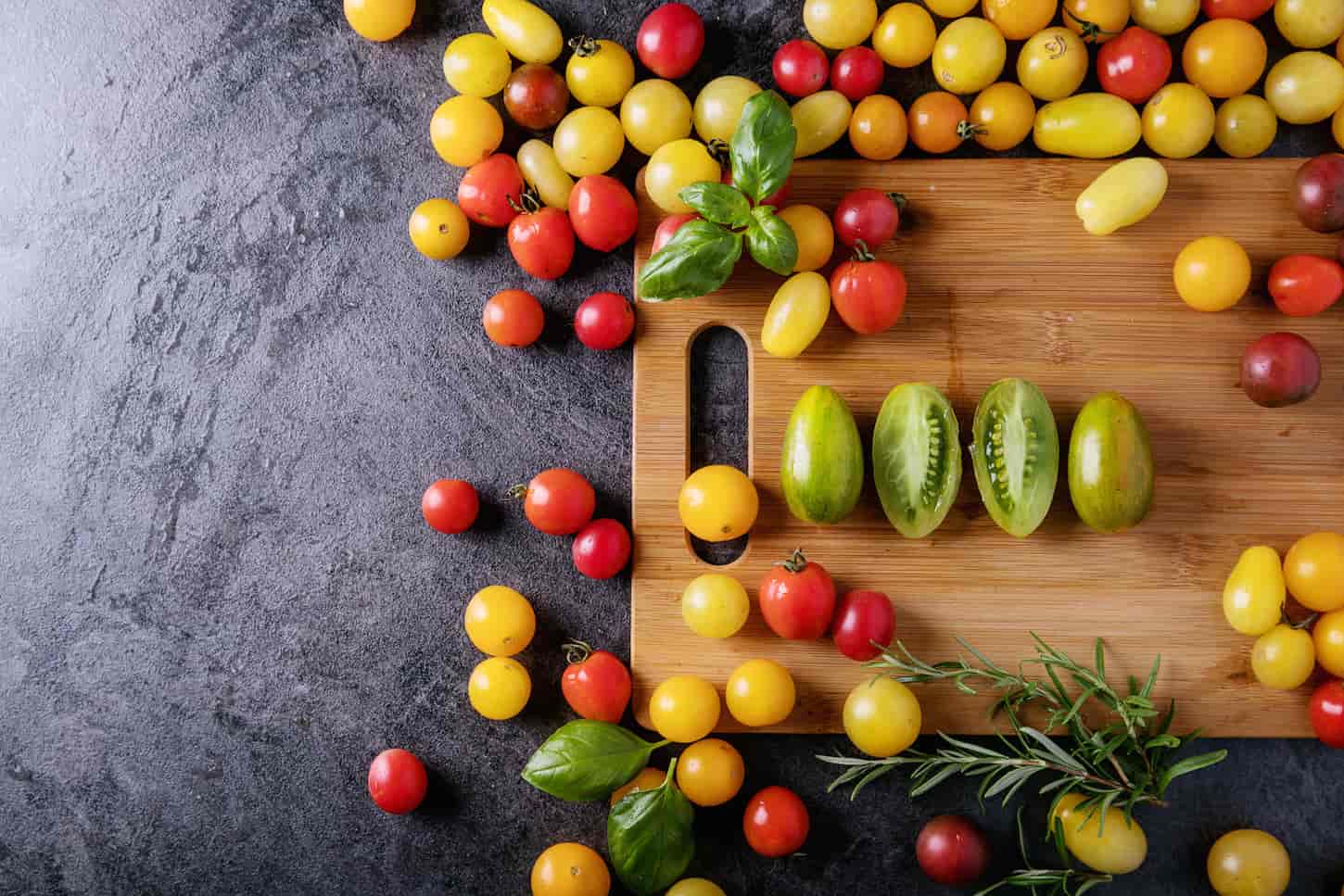 An image of cherry tomatoes: red, yellow, and green served on a wooden board over dark texture background.