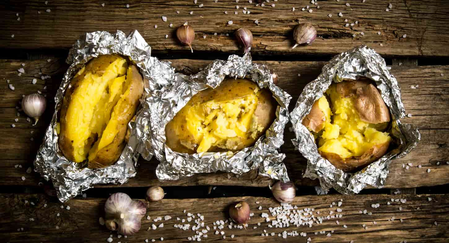 An image of Baked potatoes in foil on a wooden table.