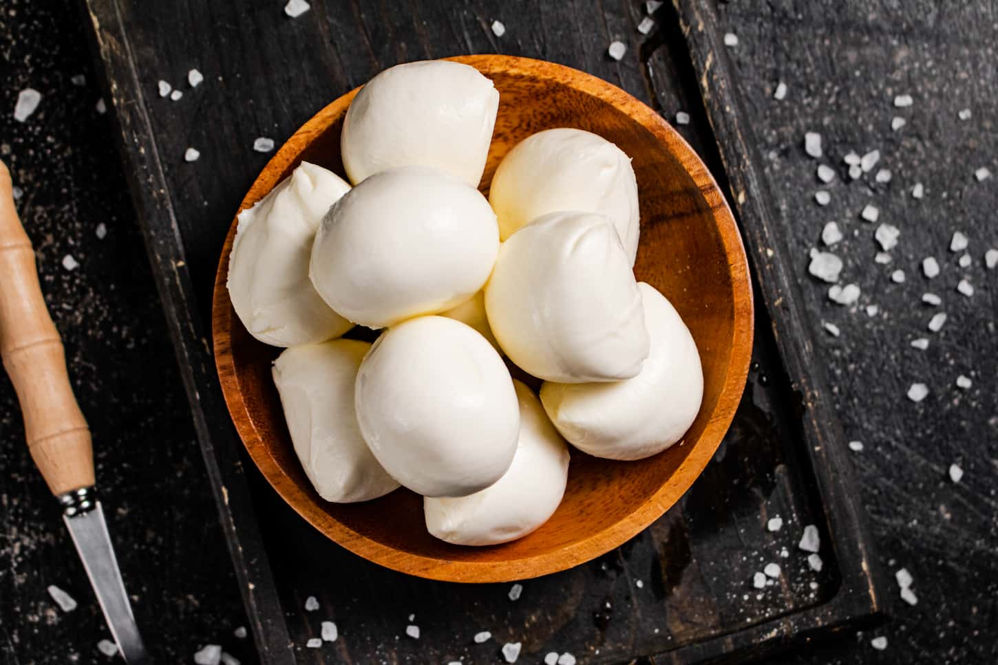 An image of mozzarella cheese on a cutting board with salt scattered on black table background.