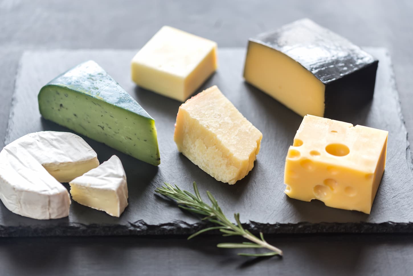 An image of Various types of cheese on the black stony board.