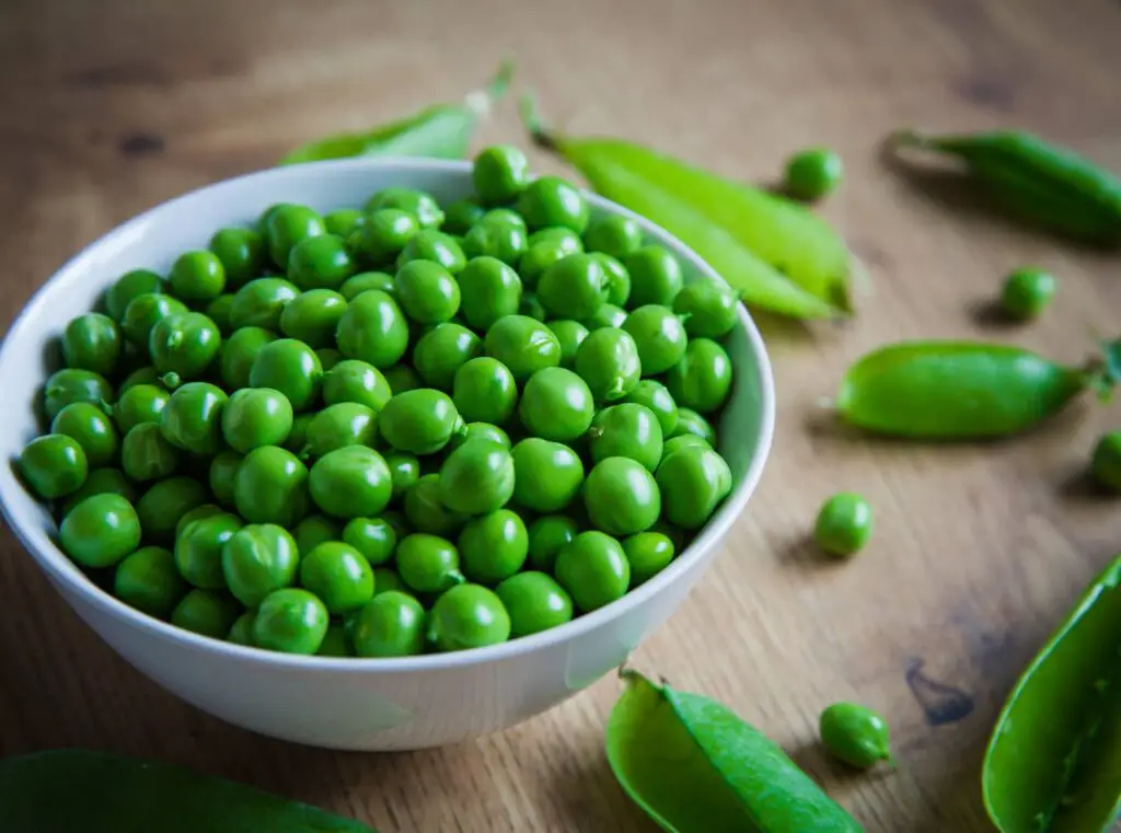 An image of a bowlful of freshly picked and podded homegrown garden peas on a wooden tabletop.