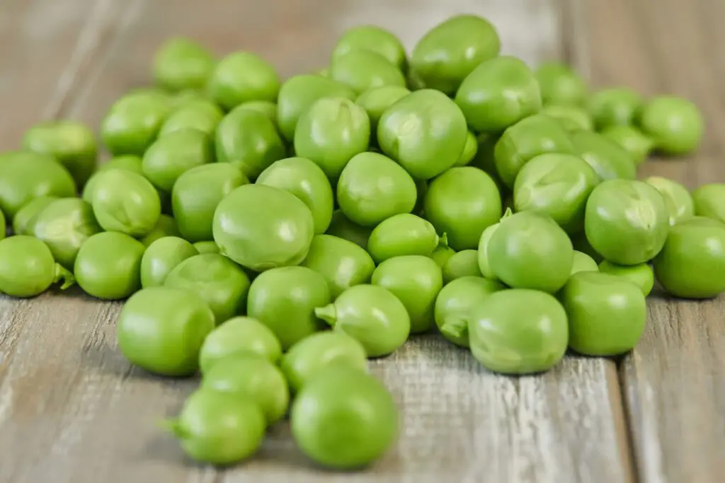 An image of Fresh green peas heap on wooden background.