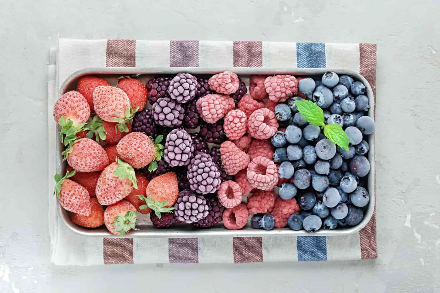 An image of Frozen berries in a metal tray on grey concrete.