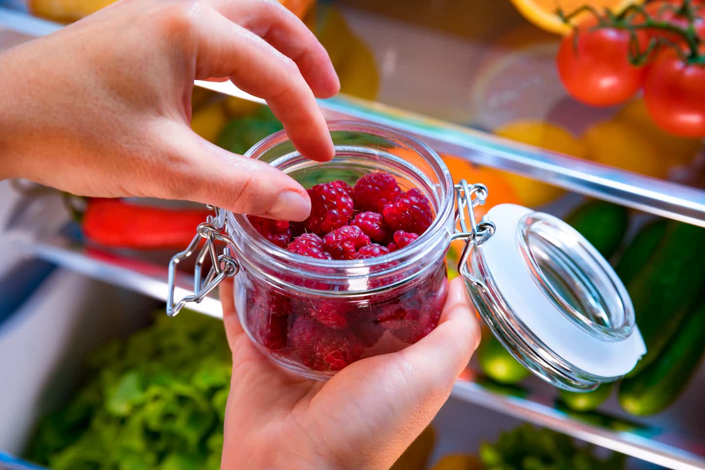 An image of a Woman taking fresh raspberries berry from the open refrigerator. Healthy food.