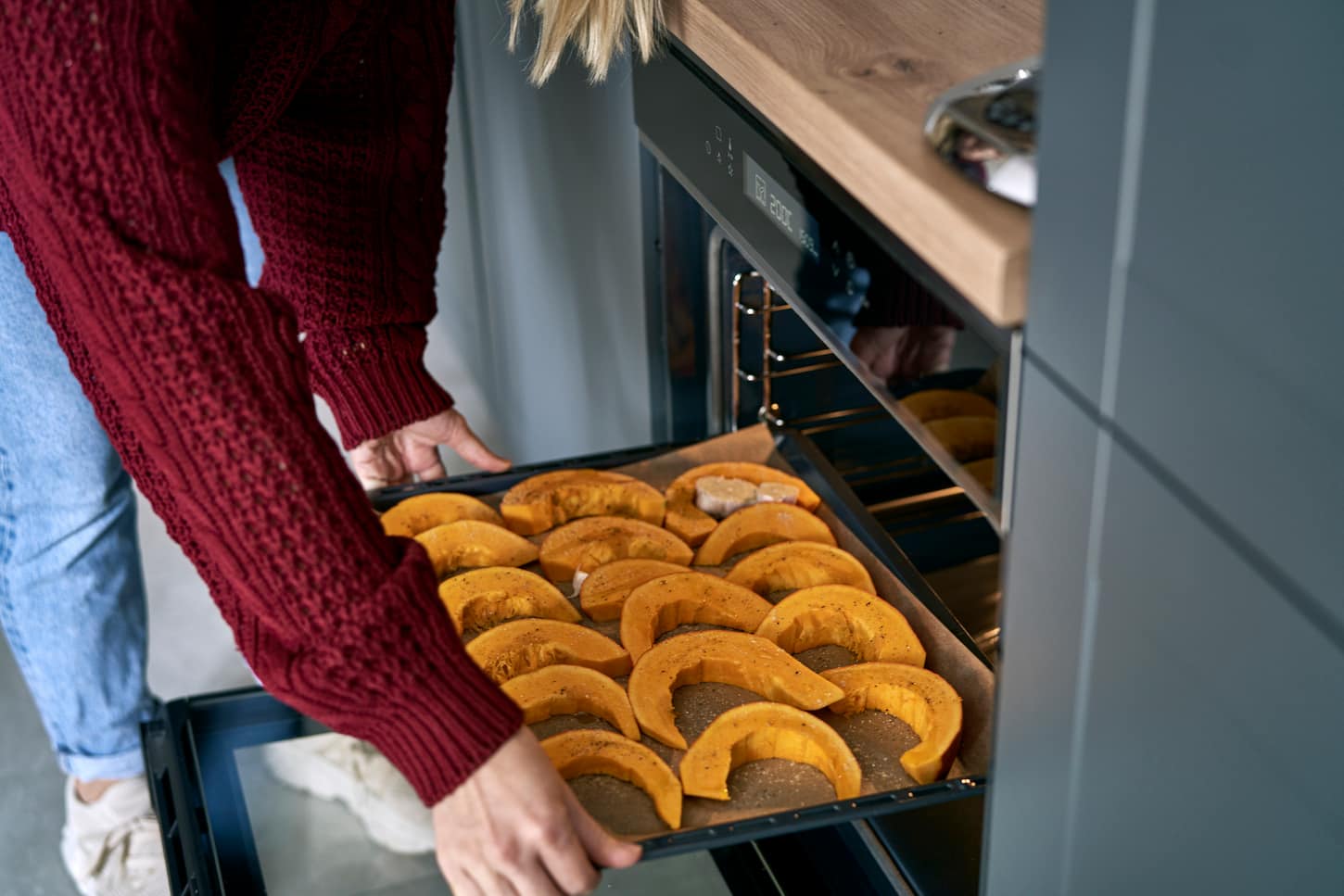 An image of a woman putting pumpkin to oven at home.