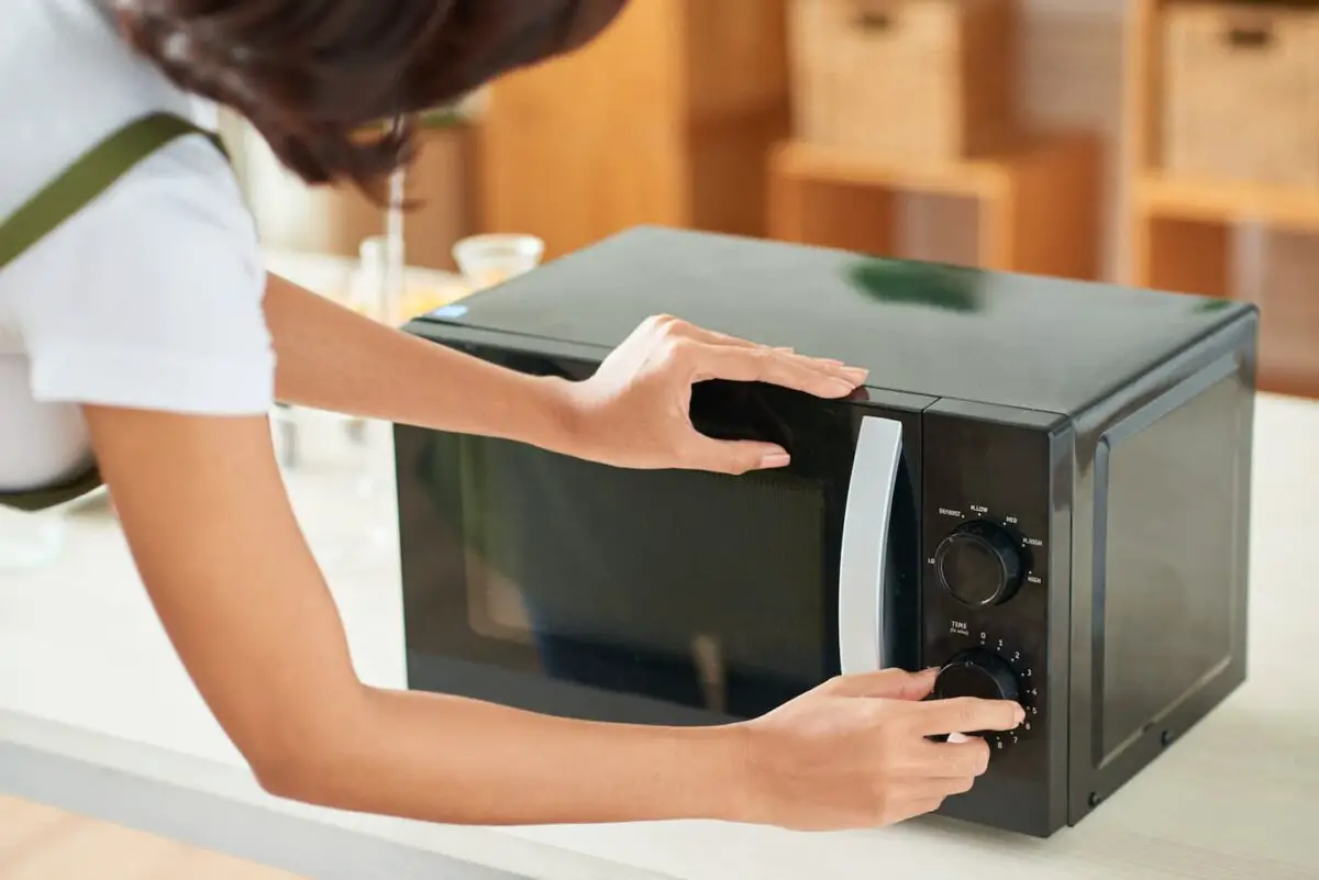 An image of a Woman Setting Time on a Microwave.