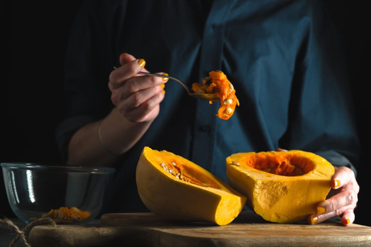 An image of a woman holding a Spoon with seeds in her hand, pumpkin halves on a table on a blue background horizontal.