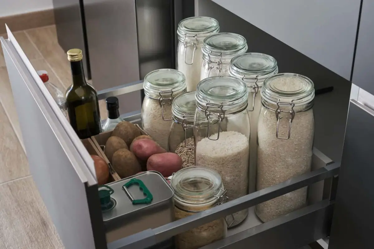 An image of a Variety of flours, packets of rice, potatoes, onion, garlic, olive oil, and vinegar in a kitchen drawer.