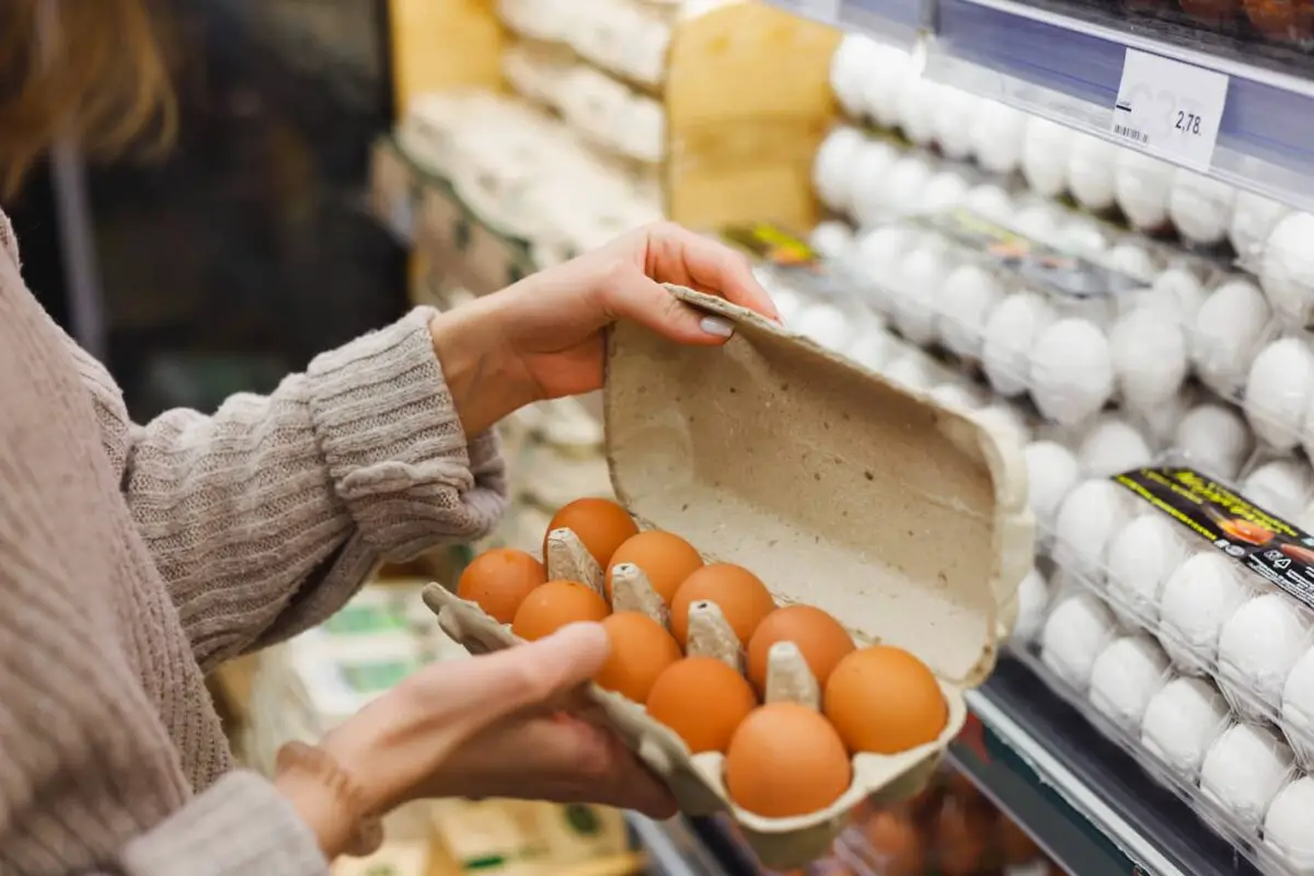An image of a Woman choosing chicken eggs in a farm food store.