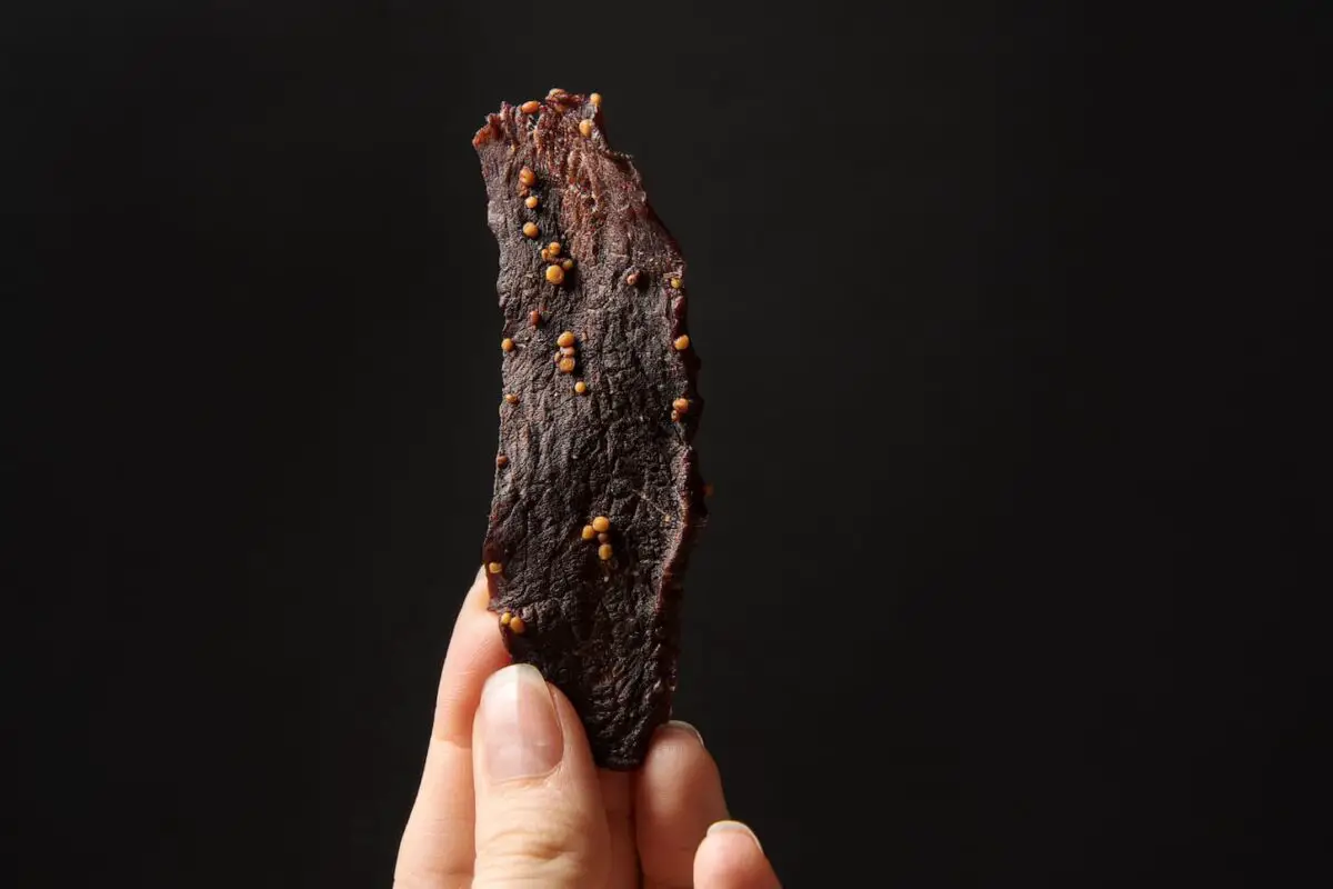 An image of a hand holding veal jerky on a black background.