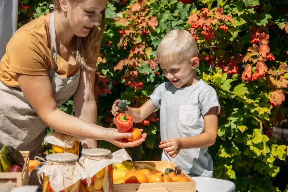 An image of a mother and her toddler canning vegetables in the garden on a summer day.