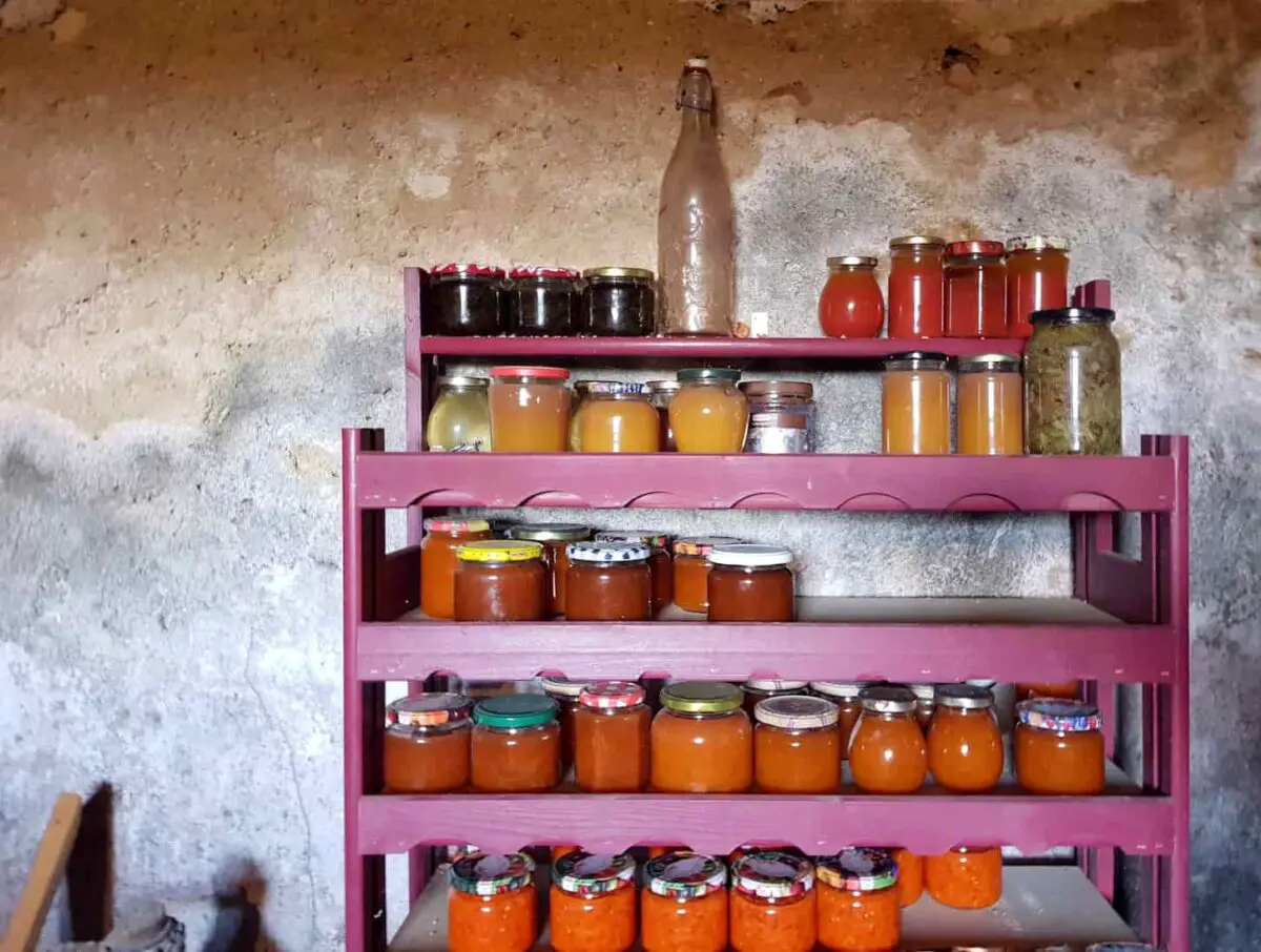 An image of Jars of Vegetables, jam, and chutney stored on a wooden rack/shelves in the cellar.