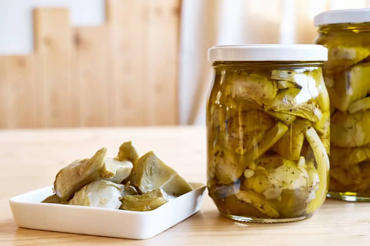 An image of Preserved fermented artichokes in olive oil in glass jars on a wooden table.