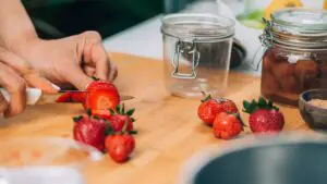 An image of a Woman Preparing Fruits cutting strawberries for Canning Preservation in the kitchen.