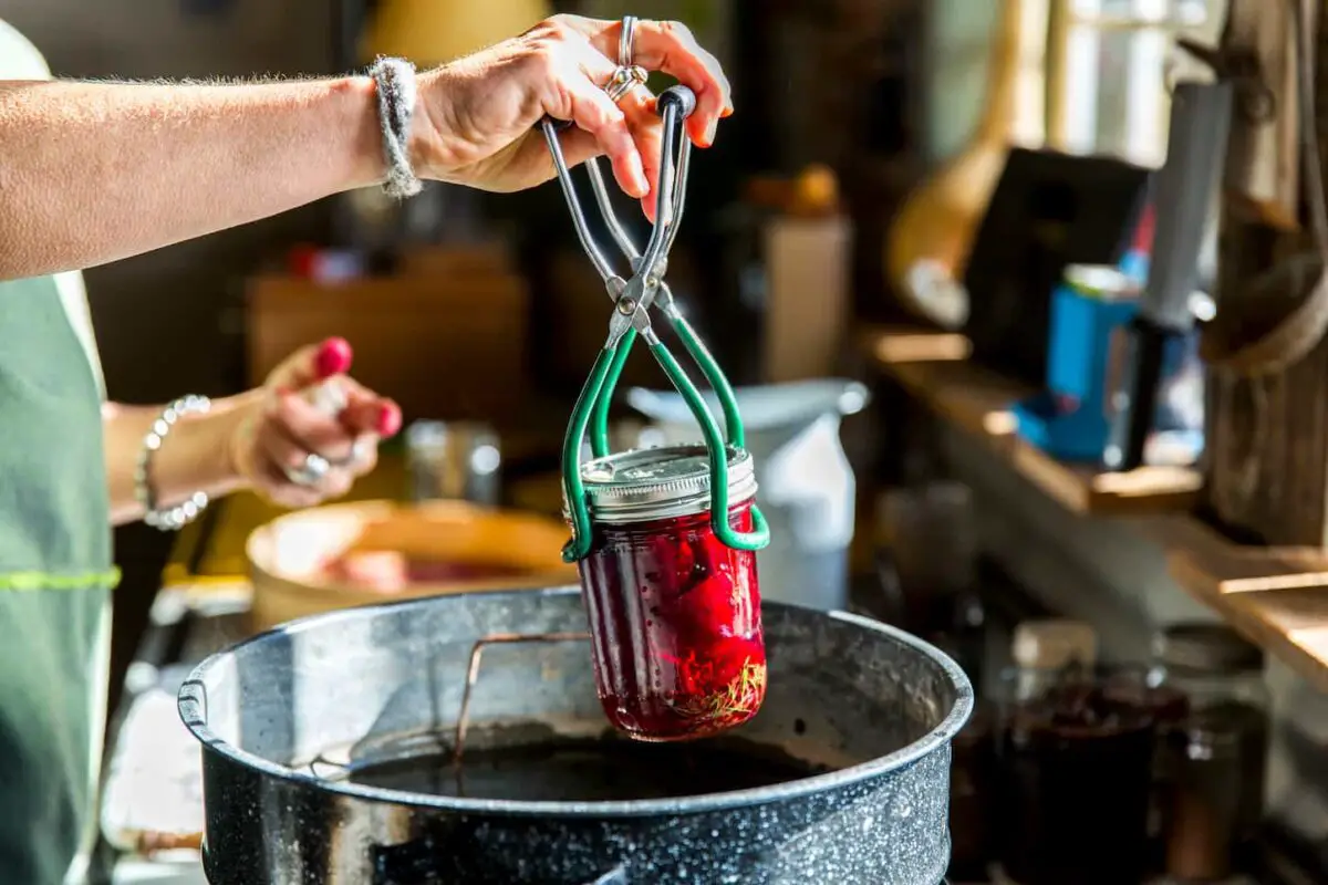 An image of a Woman's hands inserting a beetroot preserves jar into the saucepan.